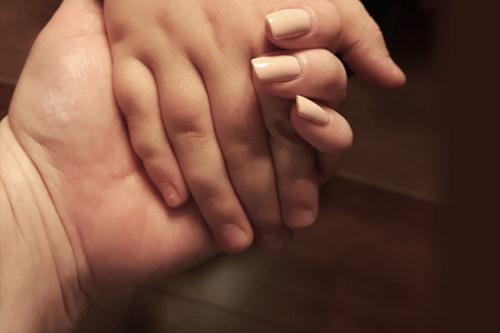Kuva käsistä. Aikuisen käsi pitää kiinni hellästi lapsen kädestä.