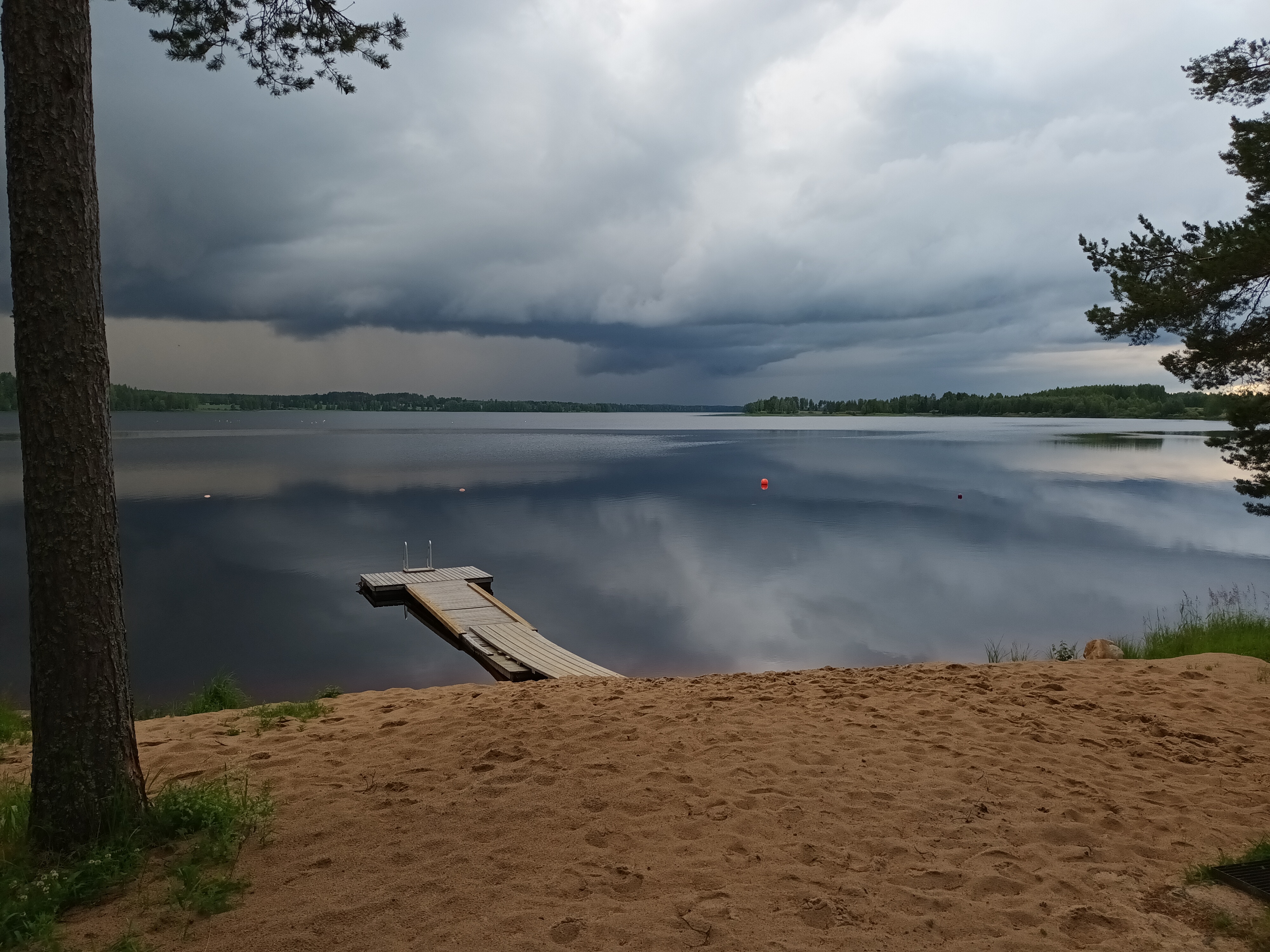 Leirikeskuksen hiekkarannan näkymä enteilee ukkosta. Järvi ja taivas ovat tummia.